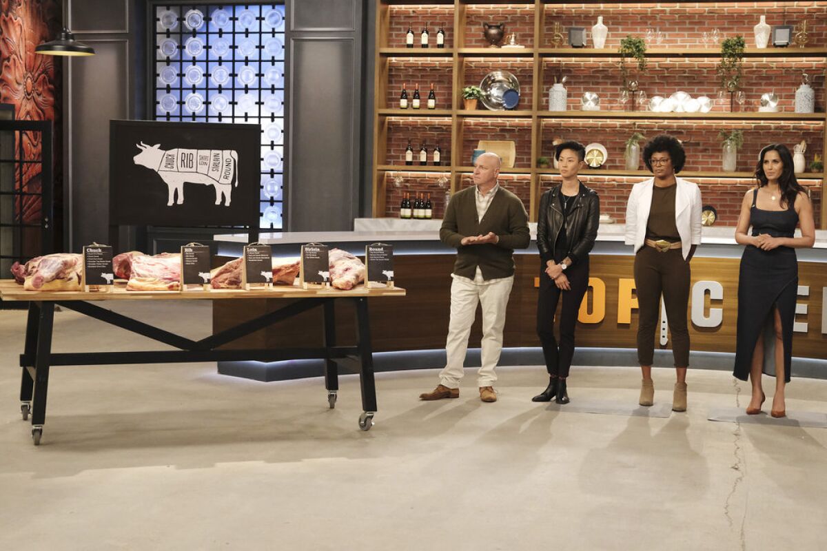 Four "Top Chef" judges stand next to a table piled with cuts of beef