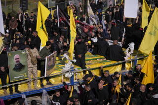 Mourners surround caskets draped with yellow flags on a flatbed truck