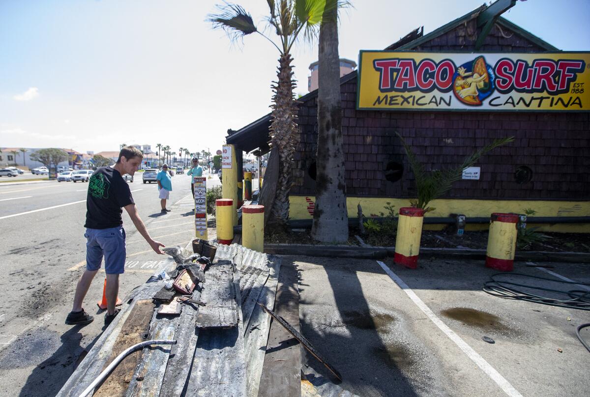 Tyler Koons tosses a piece of charred wood onto a pile outside Taco Surf in Surfside on Friday, April 15, 2022.