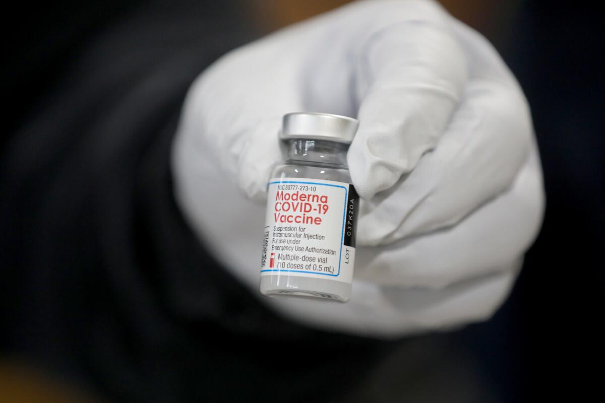 A left hand in a latex glove holding a vial of COVID-19 vaccine