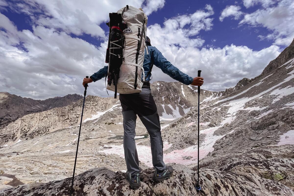 A man wearing a large backpack and carrying trekking poles gazes at mountains covered with snow. 