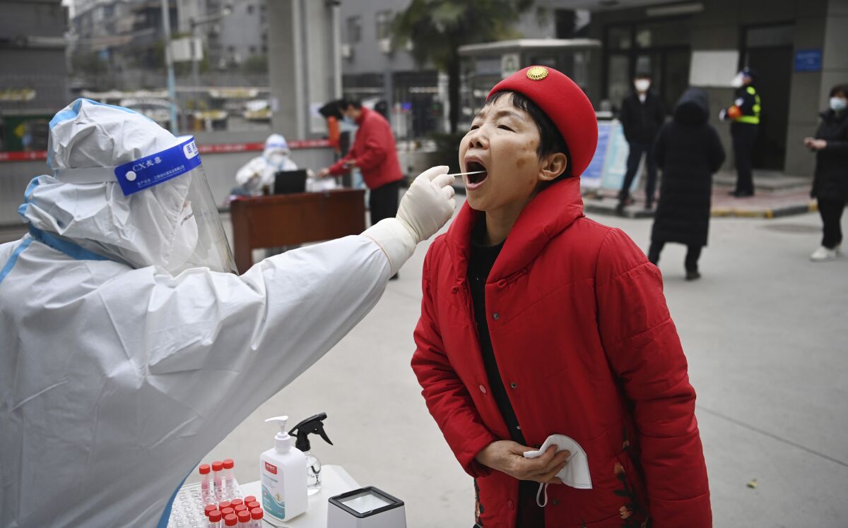 In this photo released by China's Xinhua News Agency, a worker wearing protective gear gives a COVID-19 test to a woman at a testing site in Xi'an in northwestern China's Shaanxi Province, Tuesday, Jan. 4, 2022. China is reporting a major drop in local COVID-19 infections in the northern city of Xi'an, which has been under a tight lockdown for the past two weeks. (Tao Ming/Xinhua via AP)