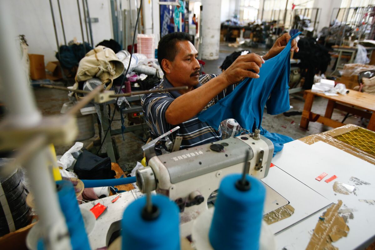 A garment worker sits by sewing machine and holds up a blue cloth
