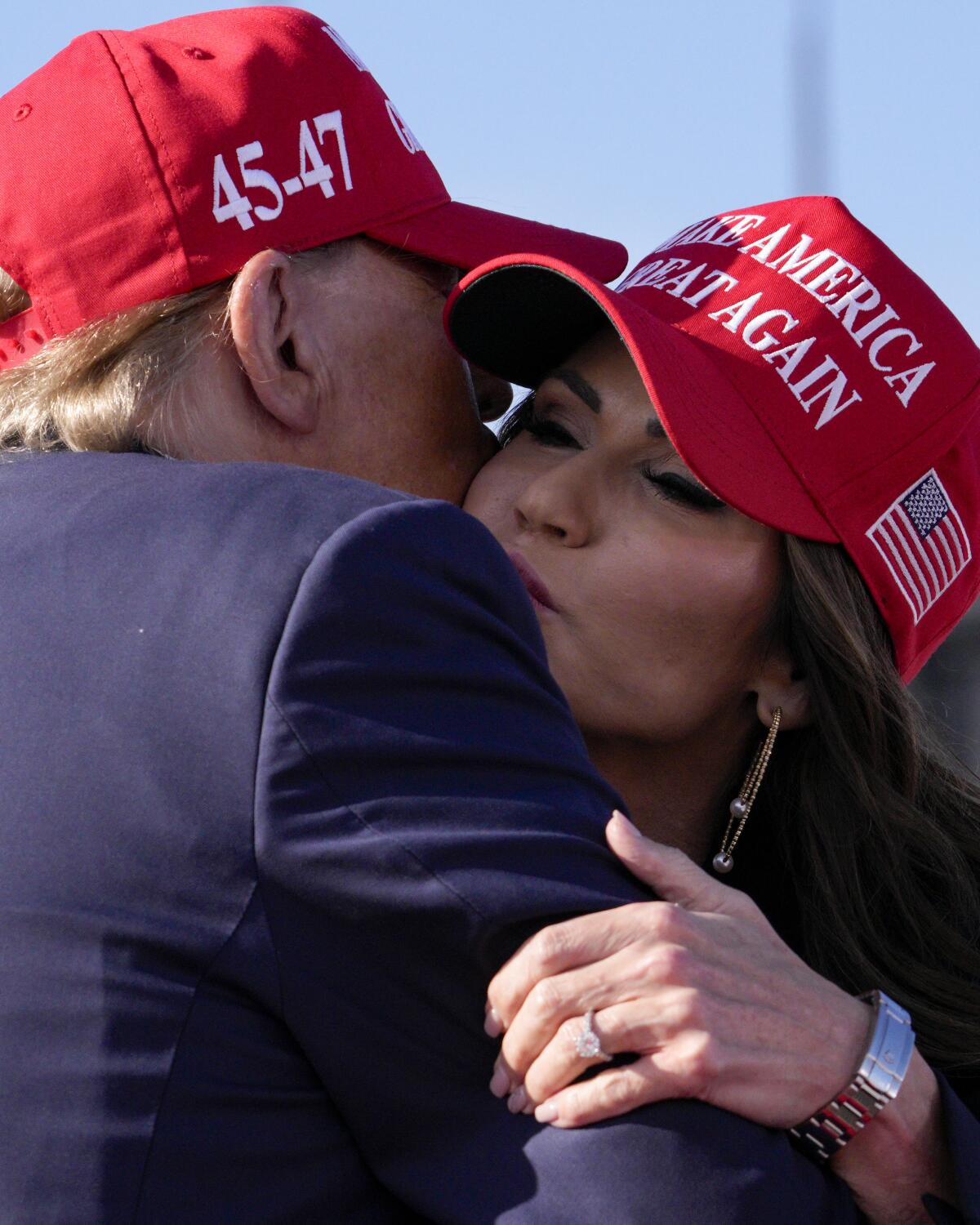 Donald Trump and Kristi Neom embrace, wearing red MAGA hats 