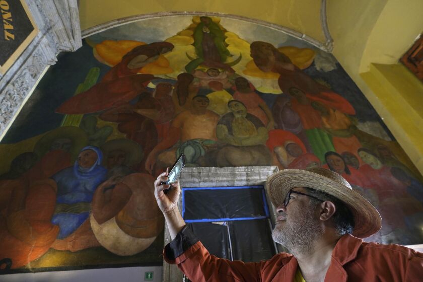 Un turista toma una foto al mural "Alegoría de la Virgen de Guadalupe" en la entrada principal del Antiguo Colegio de San Ildefonso, en la Ciudad de México, el miércoles 26 de abril de 2023. El mural fue creado por el artista mexicano Fermín Revueltas. entre 1922 y 1923, cuando los muros de San Ildefonso se convirtieron en los lienzos donde cobró vida el movimiento muralista. (Foto AP/Marco Ugarte). (AP Foto/Marco Ugarte)