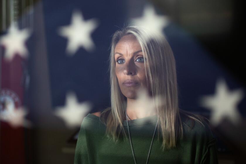 SANTA CLARITA, CA - JUNE 14: Heidi Carlon is reflected in a display case at home featuring the flag that was used to cover the body of her slain husband, firefighter Tory Carlon, who was shot to death by a fellow firefighter in June 2021 at Los Angeles County Fire Station 81 in Agua Dulce. The shooter injured a captain and then later committed suicide. Photographed in Valencia in Santa Clarita, CA on Wednesday, June 14, 2023. (Myung J. Chun / Los Angeles Times)