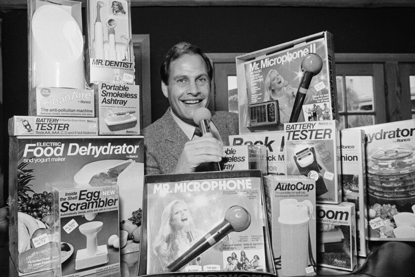 FILE - In this Wednesday, Dec. 8, 1982 file photo, Ron Popeil, the man behind those late-night, rapid-fire television commercials that sell everything from the Mr. Microphone to the Pocket Fisherman to the classic Veg-a-Matic, sits surrounded by his wares in his office in Beverly Hills, Calif. Ron Popeil, the quintessential TV pitchman and inventor known to generations of viewers for hawking products including the Veg-O-Matic, the Chop-O-Matic, Mr. Microphone and the Showtime Rotisserie and BBQ, died Wednesday, July 28, 2021 his family said. (AP Photo/Reed Saxon, File)
