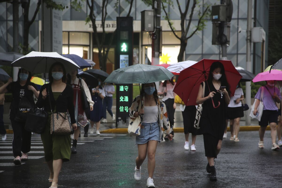 Residents using umbrellas cross an intersection in Shanghai, China, Tuesday, Sept. 14, 2021. Flights and train service were being canceled in Shanghai, China's largest city, as Typhoon Chanthu moved up the mainland coast Monday after bringing heavy rain and wind to Taiwan. (AP Photo/Chen Si)