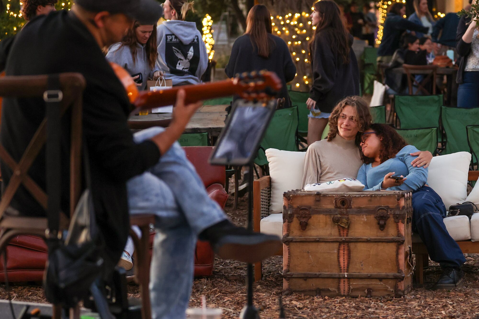 People snuggle on a couch watching a person play the guitar outdoors.