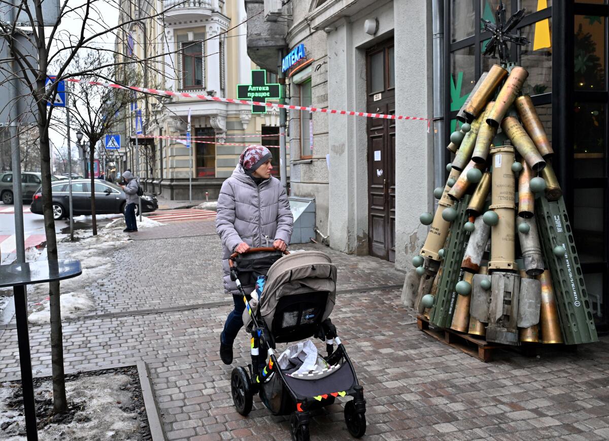 A woman pushes a pram as she walks past a symbolic Christmas tree made from spent shell casings 