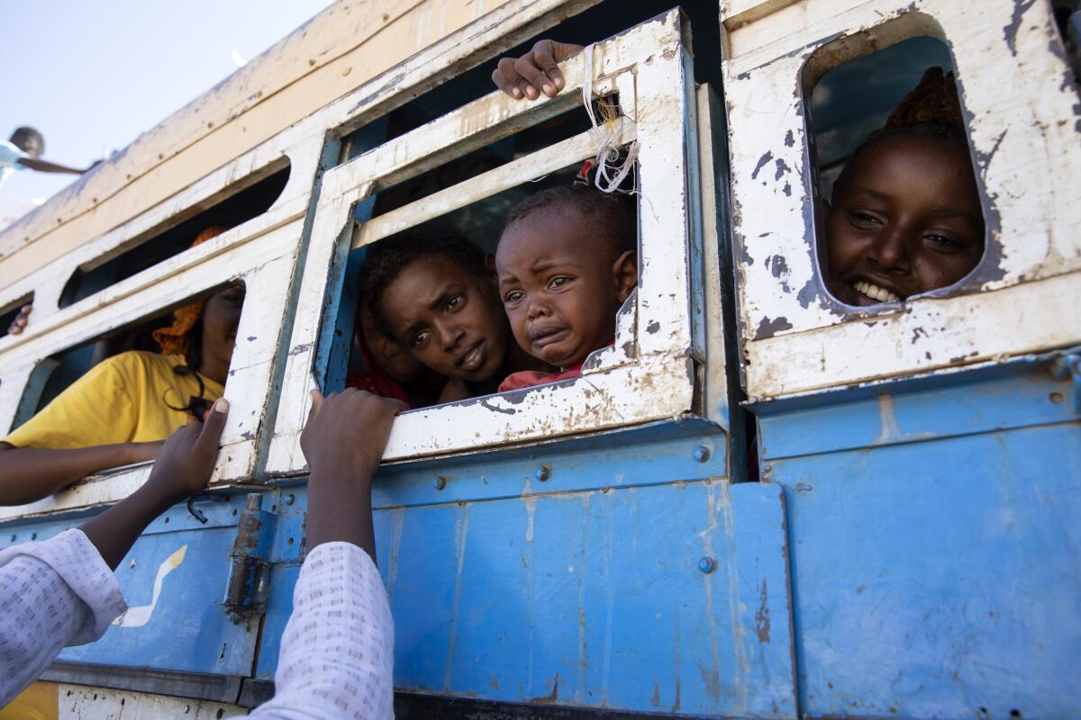 Children look out the windows of a bus while hands reach up to them