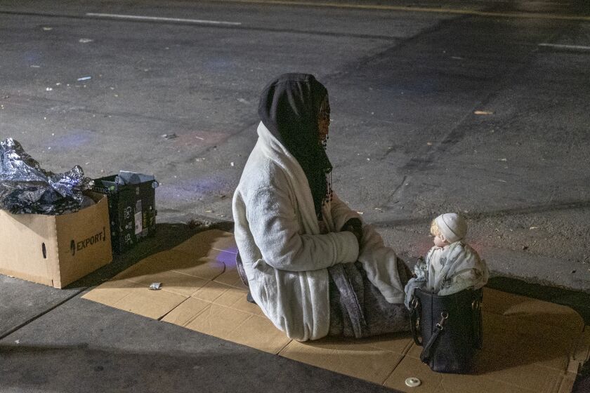 LOS ANGELES, CA - APRIL 22: A woman sits next to a doll balanced on her purse on the sidewalk in the skidrow area in the early morning hours Thursday, April 22, 2021 in Los Angeles, CA. (Francine Orr / Los Angeles Times)