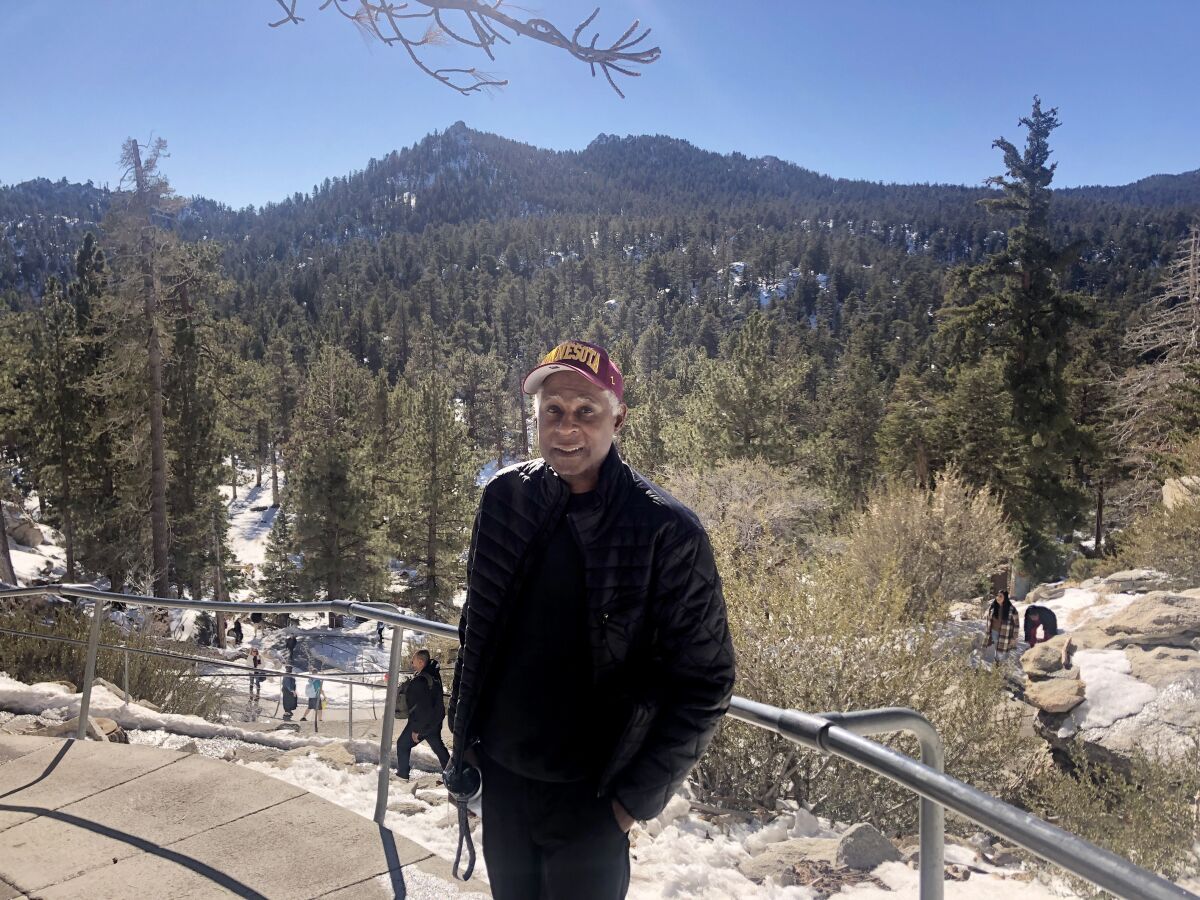 A man smiles in front of a snowy mountain landscape.