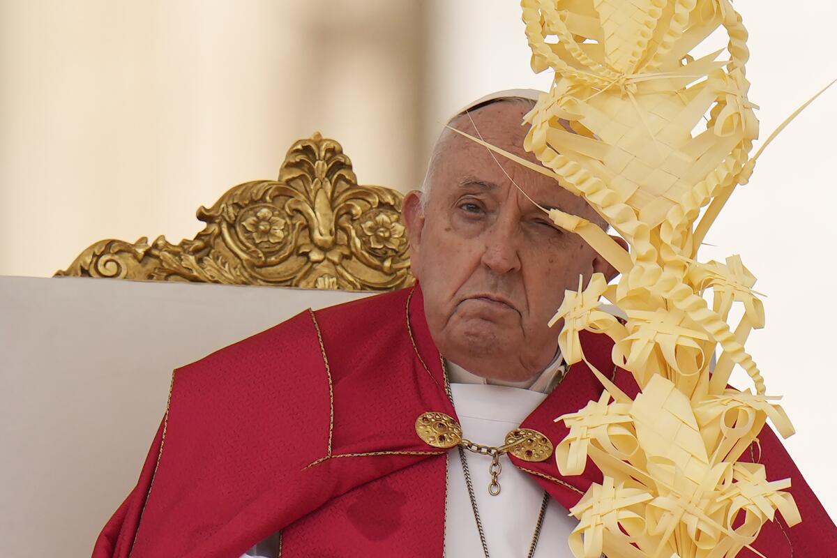 Pope Francis sits on an ornate chair while wearing red and white vestments.