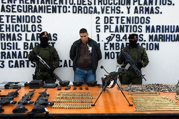 Mexican soldiers flank a suspect behind a table of weapons confiscated during a shootout in Tijuana.