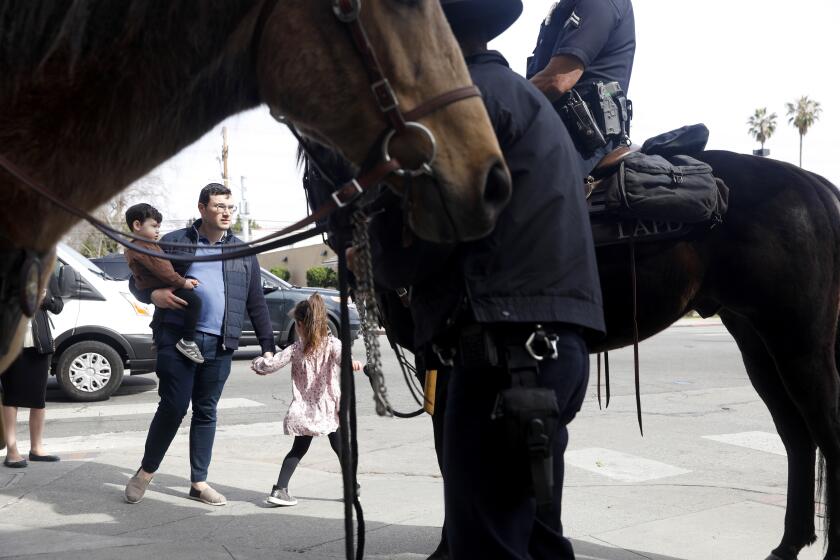 LOS ANGELES-CA-FEBRUARY 17, 2023: Izik Goldstein, visiting from London, with children Akiva, 3, and Tali, 5, right, pass by LAPD officers on horseback along Pico Boulevard in the Pico-Robertson area of Los Angeles on Thursday, February 17, 2023, after the recent shootings of two Jewish men. (Christina House / Los Angeles Times)