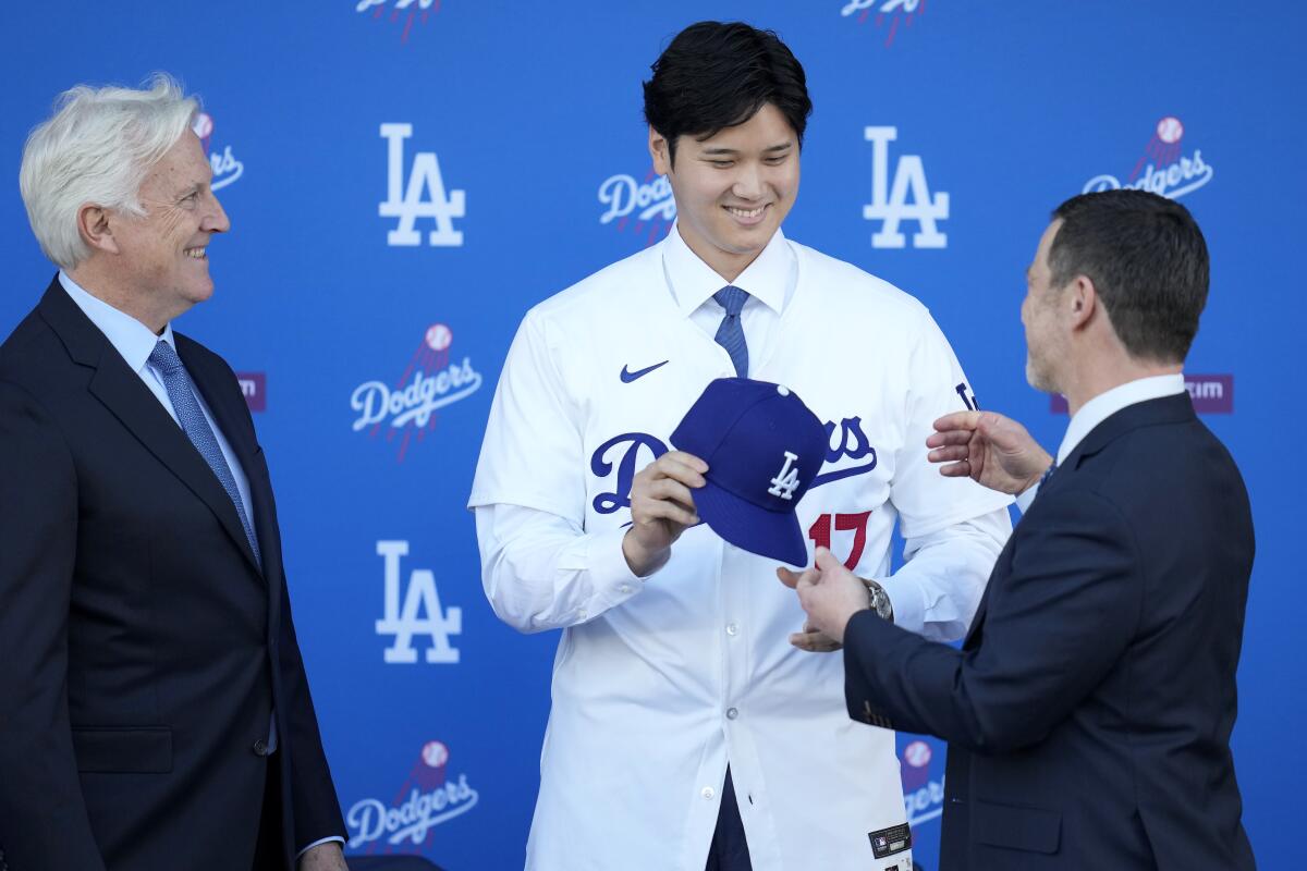 Shohei Ohtani recibe una gorra de manos de Andrew Friedman, presidente de operaciones deportivas