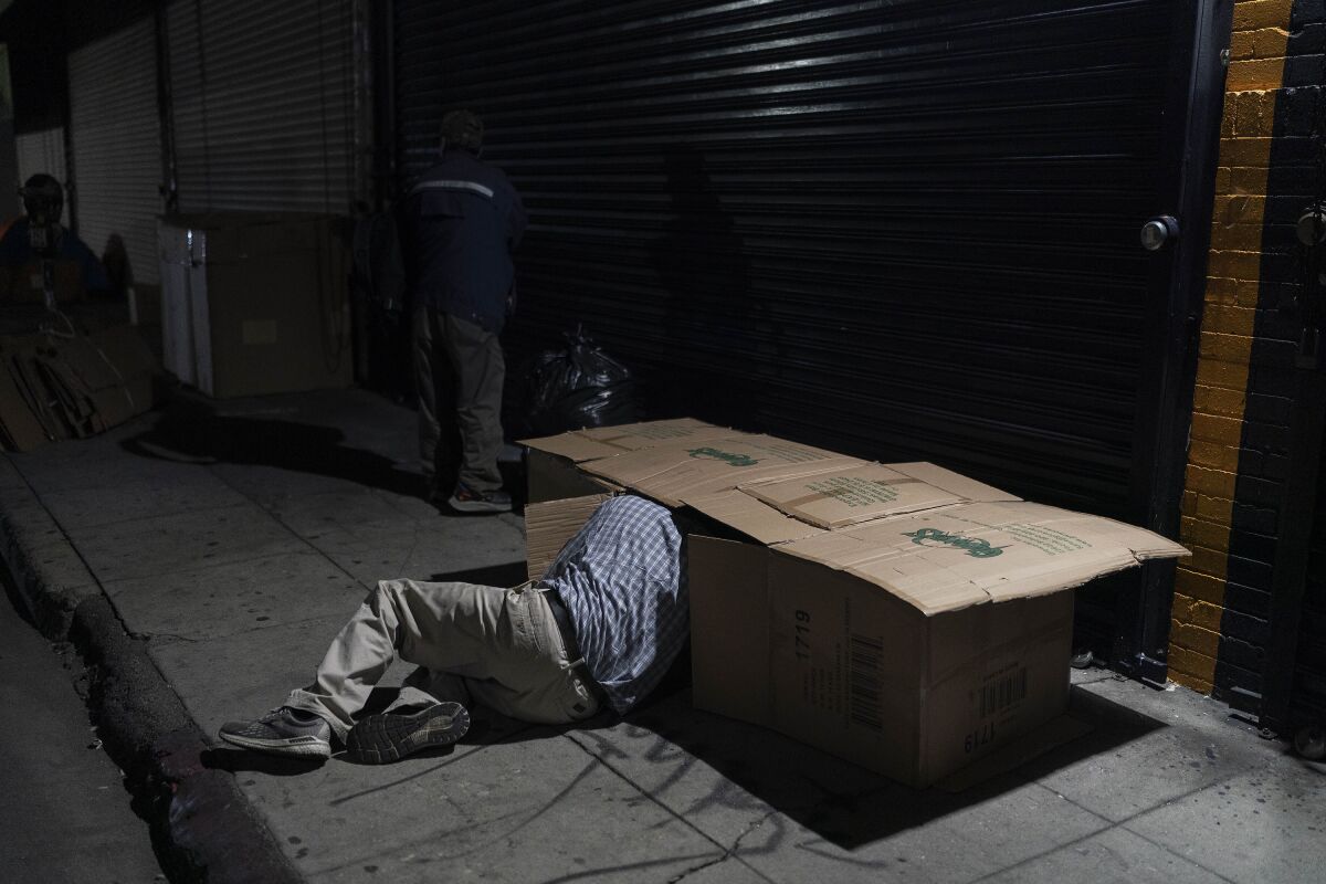 A homeless man crawls into a bed made with cardboard boxes in Los Angeles.