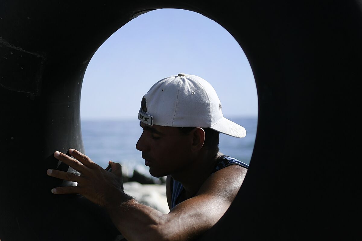 Larry Jimenez, 34, inflates his inner tube in preparation for open sea fishing, at Playa Escondida in La Guaira, Venezuela, Friday, Aug. 14, 2020, amid the new coronavirus pandemic. Venezuelans like Jimenez have turned to fishing the high sea on salvaged inner tubes for survival as the nationwide lockdown paralyzes an already crumbling economy and eliminates their jobs in construction and restaurants. (AP Photo/Matias Delacroix)