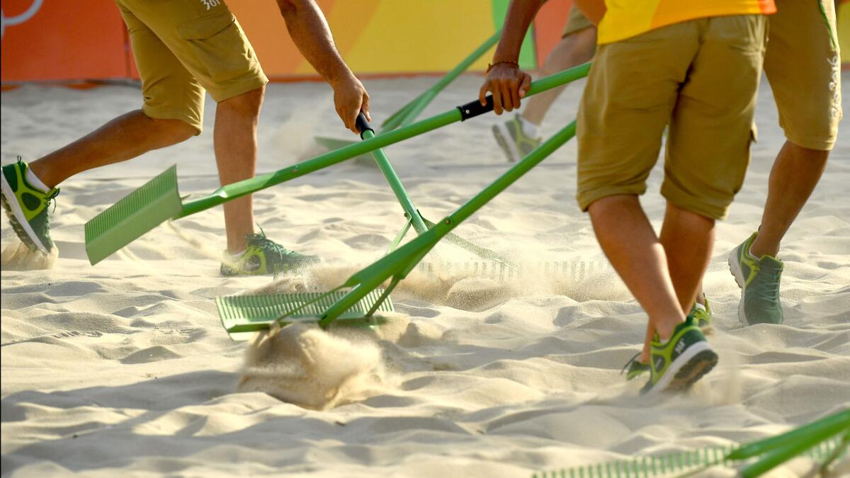 Volunteers rake the court during the women's beach volleyball qualifying match between Brazil and the Czech Republic.