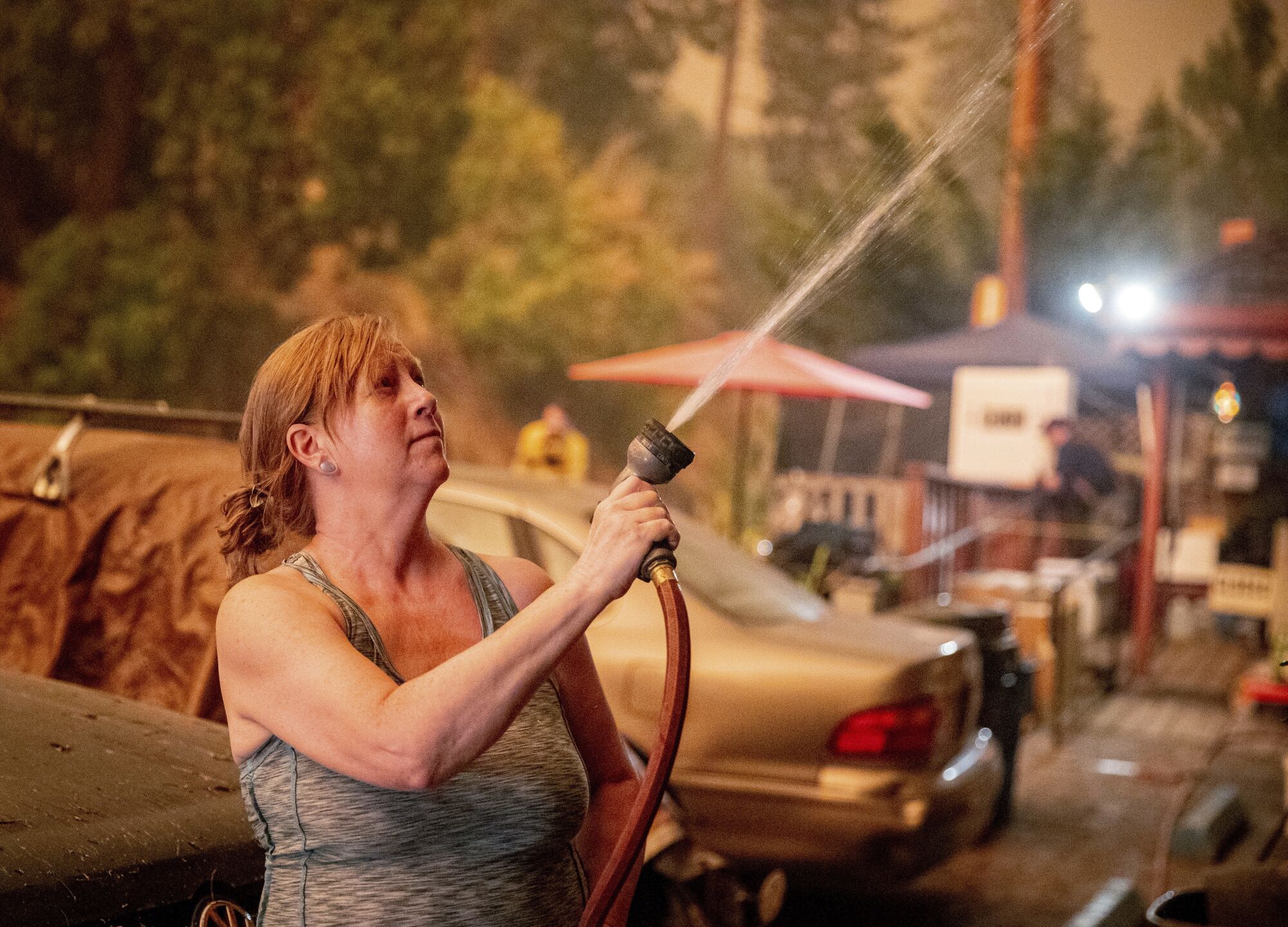 A woman sprays a hose at her house in smoky air