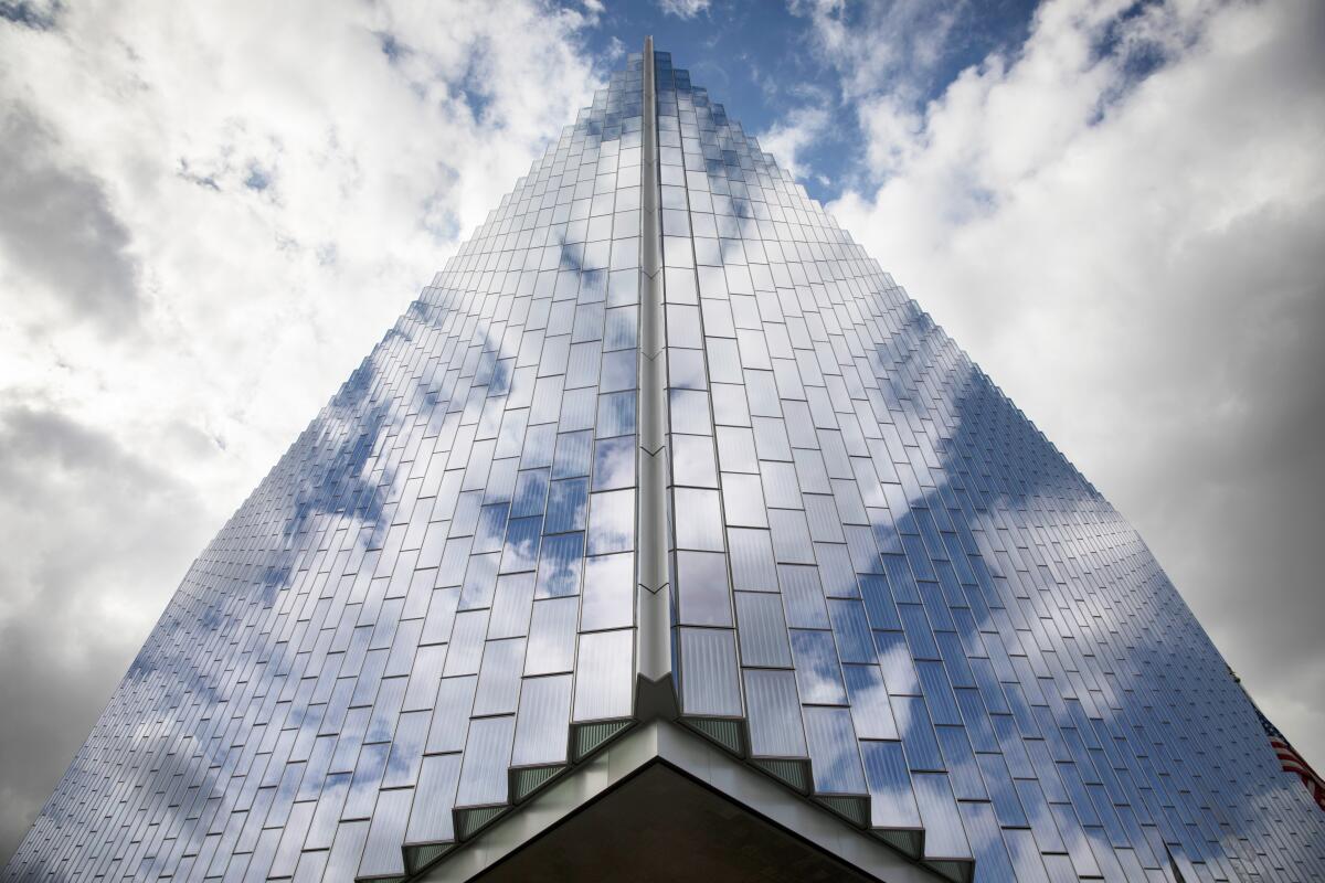 Clouds reflect off a building that towers into the sky.