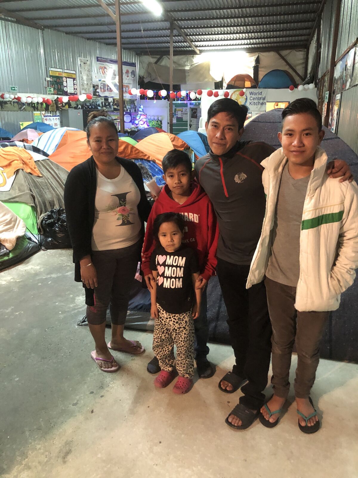 A family poses in front of tents inside a concrete-floored room