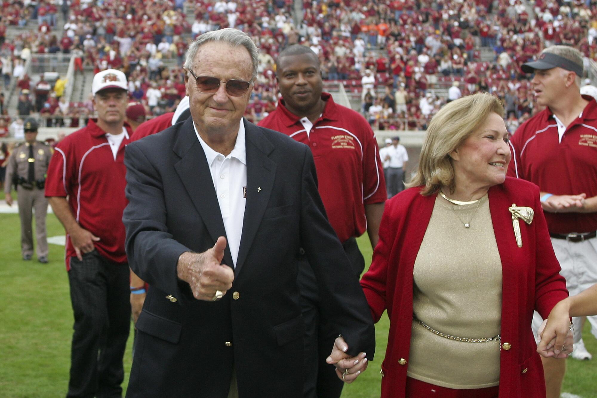 Former Florida State coach Bobby Bowden, holding hands with his wife Ann, gives a thumbs up 