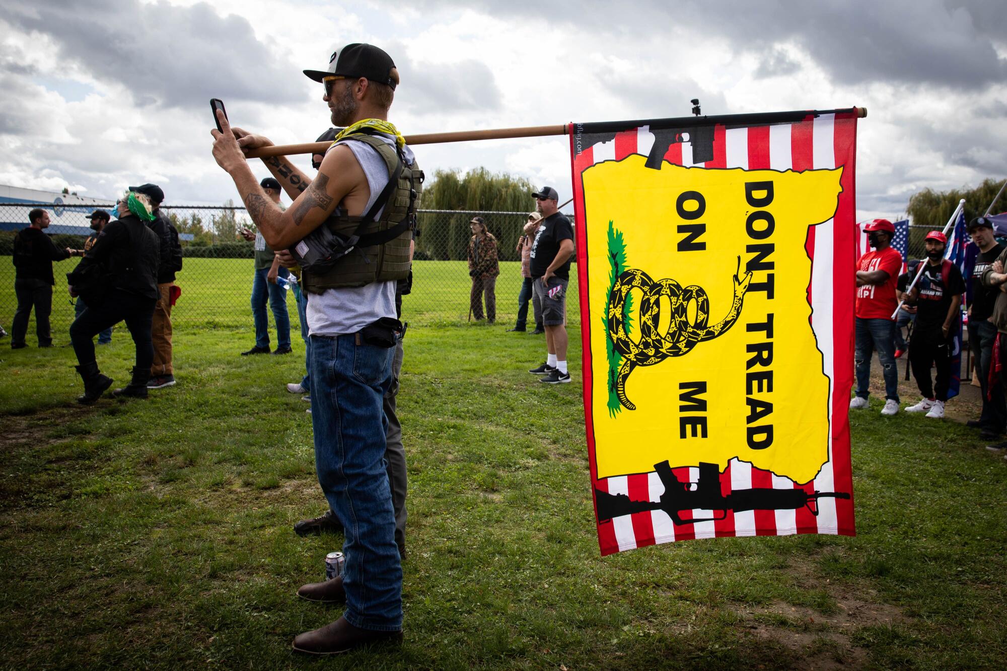 A man holds a "Don't tread on me" flag in the shape of Oregon with images of assault rifles on either side