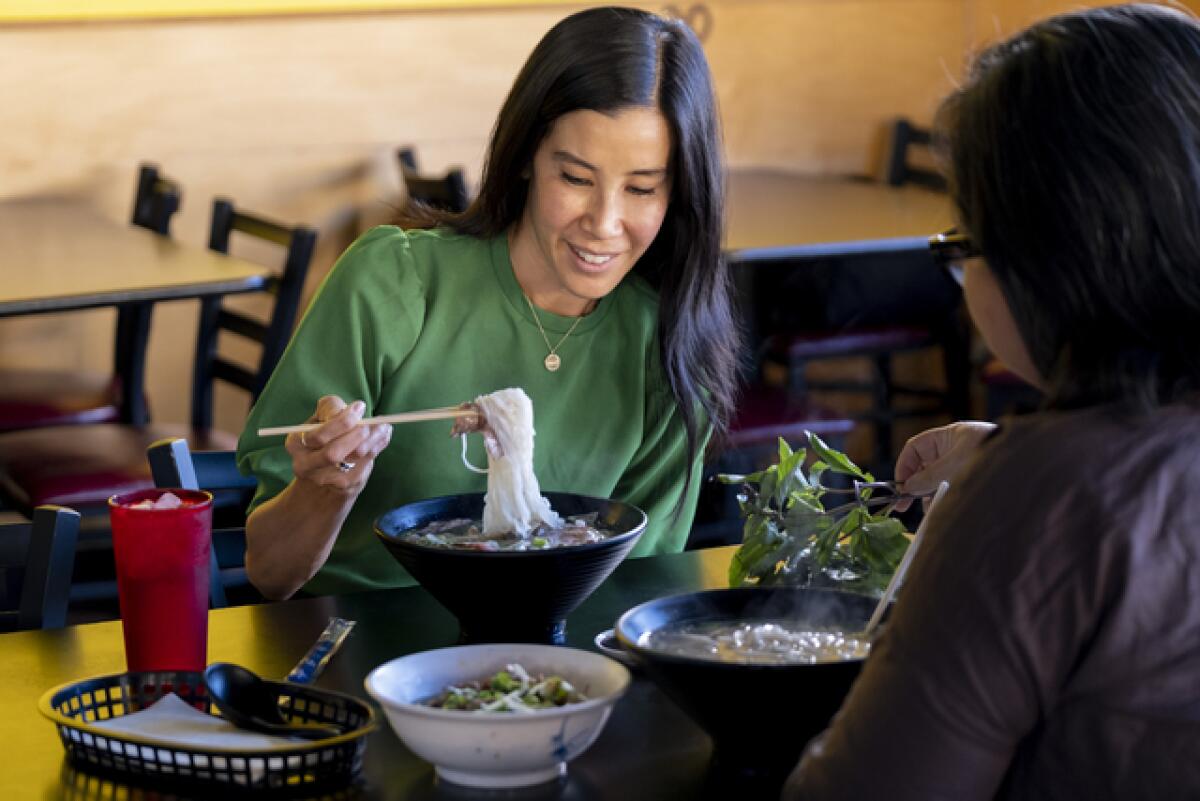 A woman in a green shirt twirls noodles in a bowl with chopsticks.