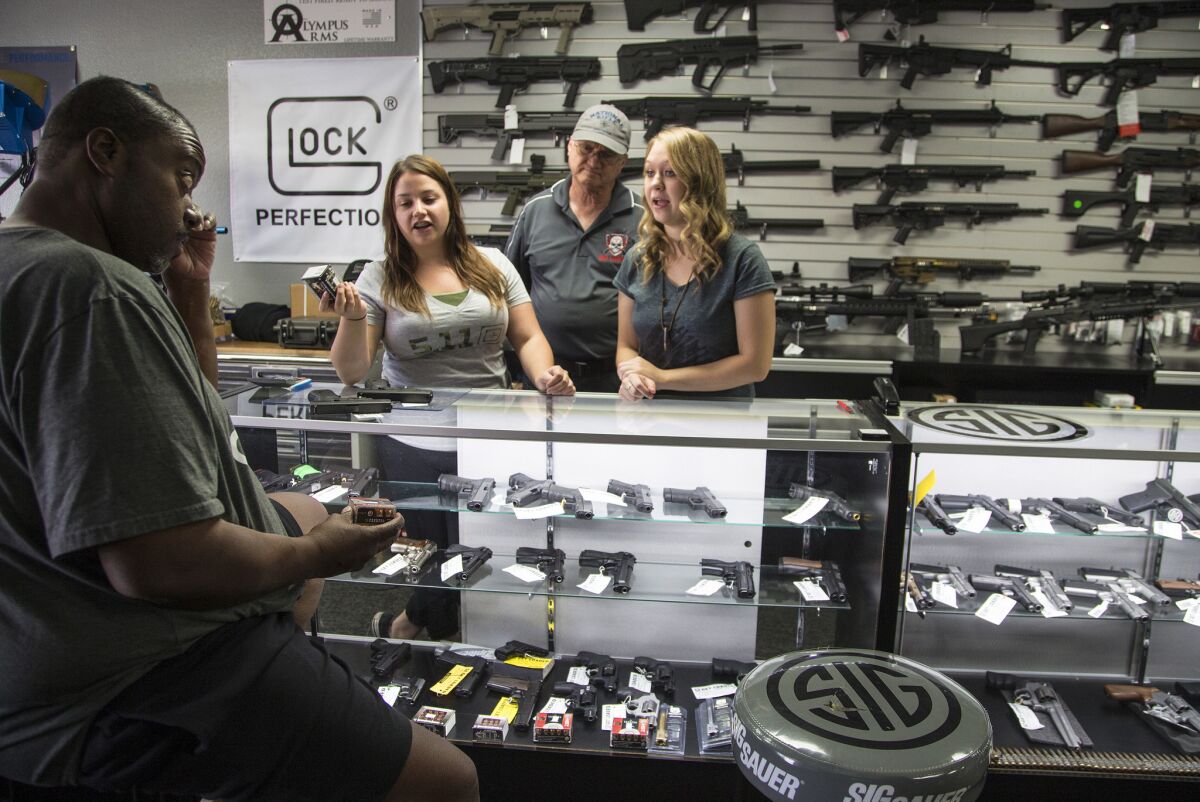 Store managers Jamie Taflinger, left, and Kendyll Murray serve customer Cornell Hall of Highland at the Get Loaded gun store in Grand Terrace, which has seen a surge in gun sales ahead of the Jan. 1 implementation of new laws.