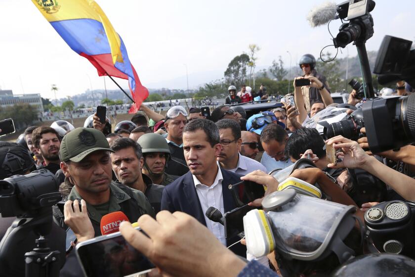 Venezuela's opposition leader and self-proclaimed president Juan Guaido, center, stands with an unidentified military officer who is helping to lead a military uprising, center left, as they talk to the press and supporters outside La Carlota air base in Caracas, Venezuela, Tuesday, April 30, 2019. Guaid?? took to the streets with activist Leopoldo Lopez and a small contingent of heavily armed troops early Tuesday in a bold and risky call for the military to rise up and oust Maduro. (AP Photo/Fernando Llano)