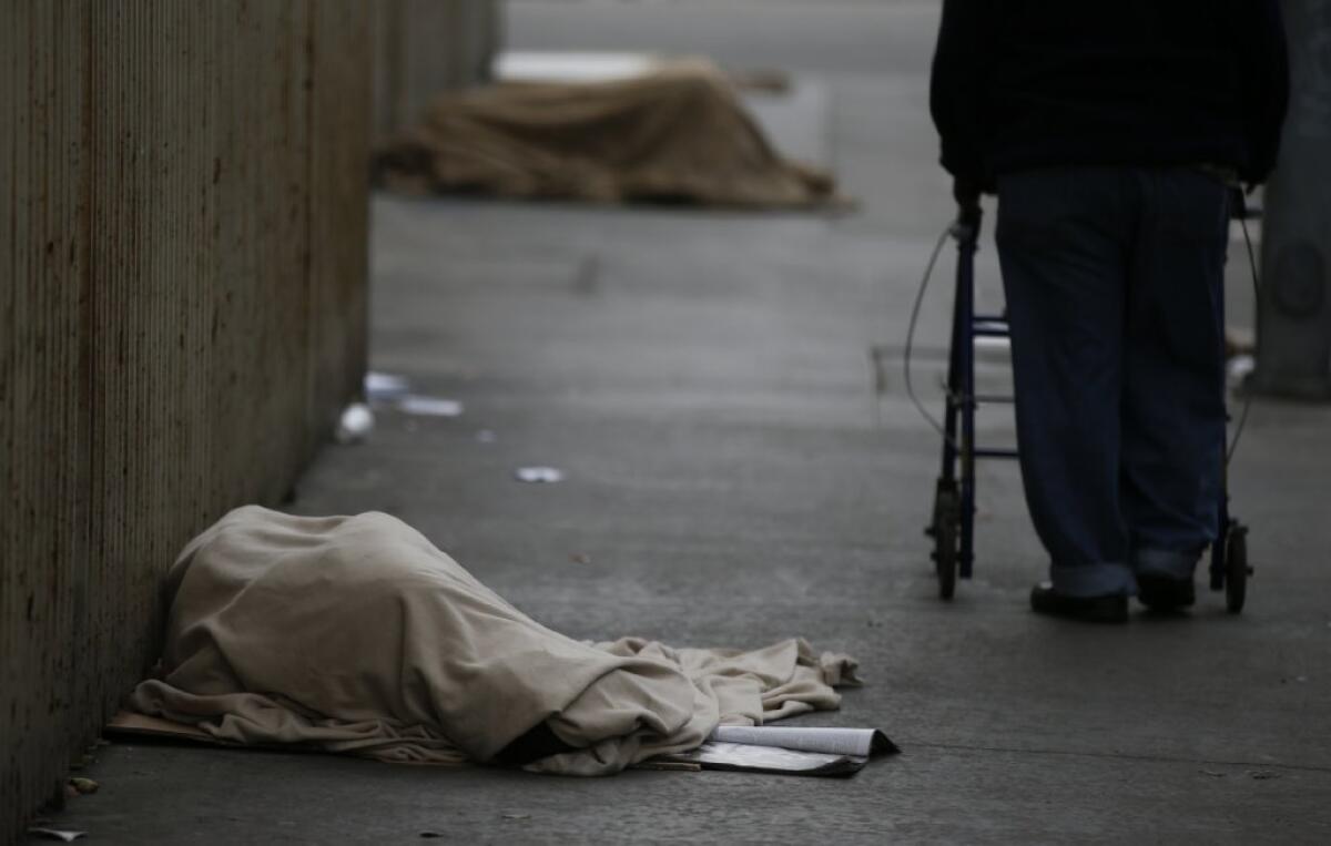 Homeless men and women draped in blankets sleep on the sidewalk along Wall Street in downtown Los Angeles in January.