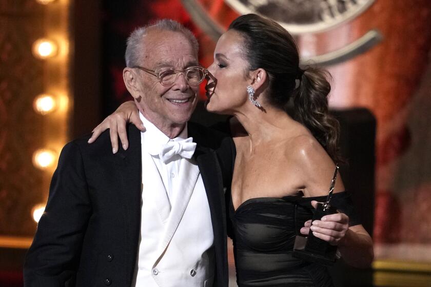 Jennifer Grey in a black dress kisses her father Joel Grey on the cheek as he wears a black and white tuxedo onstage