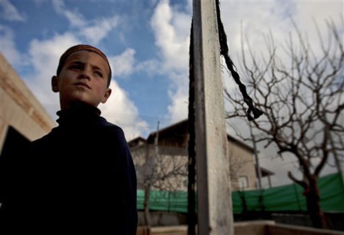 In this photo taken Wednesday, Feb. 9, 2011 a Palestinian boy stands in the yard of the fenced-in house of al-Ghirayim family between the Jewish settlement of Givon Hahadasha and the West Bank village of Beit Ijza. The al-Ghirayib family lives in one of the stranger manifestations of Israel's 43-year occupation of the West Bank: a Palestinian house inside a metal cage inside an Israeli settlement. The family's 10 members, four of them children, can only reach the house via a 40-yard (meter) passageway connecting them to the Arab village of Beit Ijza below. The passage passes over a road frequented by Israeli army jeeps and is lined on both sides with a 20-foot-high (6-meter) heavy-duty metal fence.(AP Photo/Sebastian Scheiner)