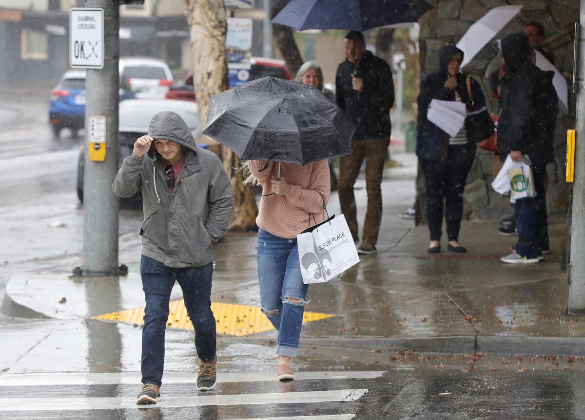Visitors duck under umbrellas, jackets, and awnings at Coast Highway and Laguna Avenue  in Laguna Beach Monday morning.