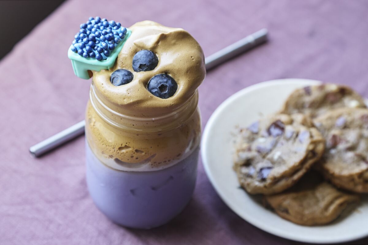 Blueberry Dalgona Coffee, topped with blueberries, is adorned with a Mug Buddy Cookie.