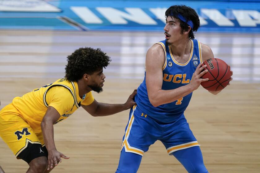UCLA guard Jaime Jaquez Jr. (4) looks to pass over Michigan guard Mike Smith, left, during the first half of an Elite 8 game in the NCAA men's college basketball tournament at Lucas Oil Stadium, Tuesday, March 30, 2021, in Indianapolis. (AP Photo/Michael Conroy)