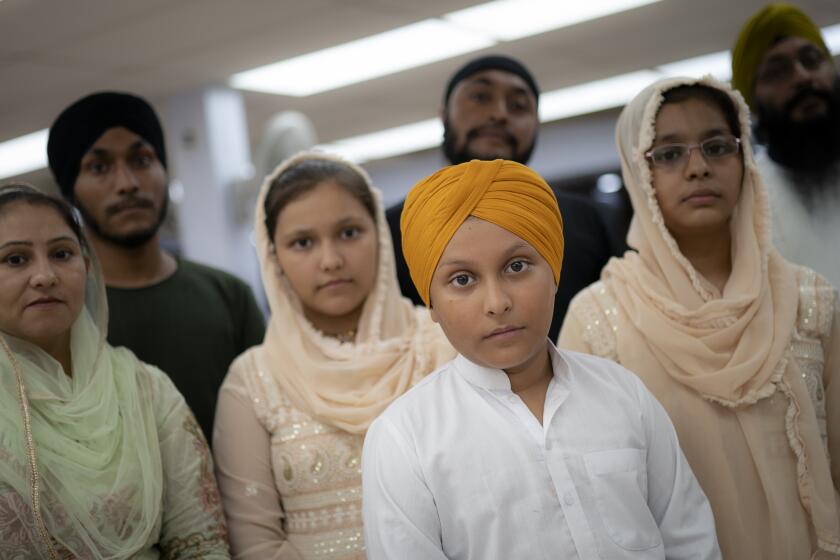 Amandeep Singh, 12, stands with his family in the communal room where "langar," food served after temple services, is provided at Guru Nanak Darbar of Long Island, a Sikh gurdwara, Wednesday, Aug. 24, 2022, in Hicksville, N.Y. Their Afghan Sikh family of 13 has found refuge in the diaspora community on Long Island where the Sikh community is helping family members obtain work permits, housing, healthcare and find schools for the children. (AP Photo/John Minchillo)
