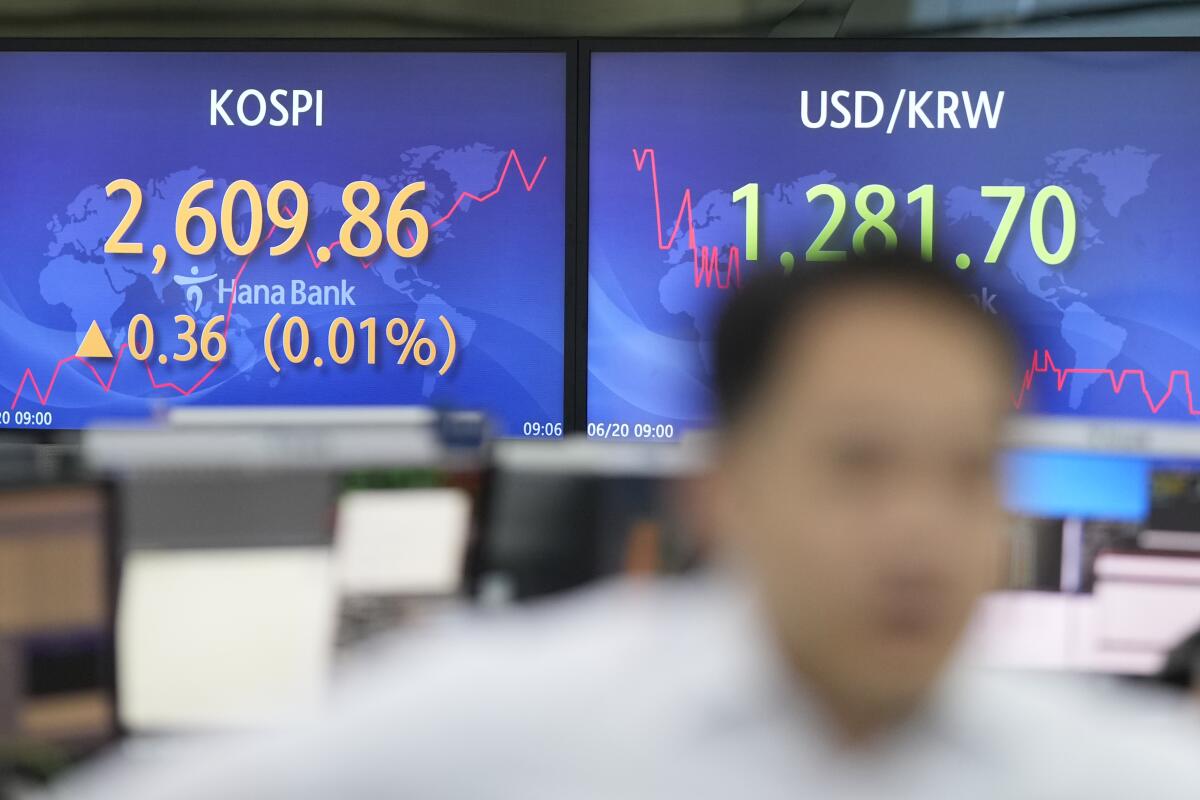 A blurred image of a currency trader walking by the screens showing the Korea Composite Stock Price Index (KOSPI)