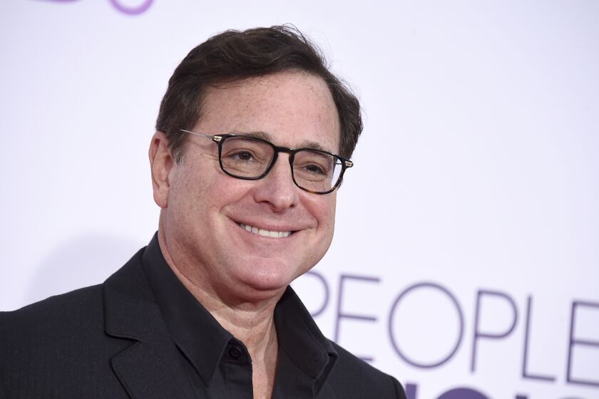 Bob Saget smiling in a glasses and a black suit