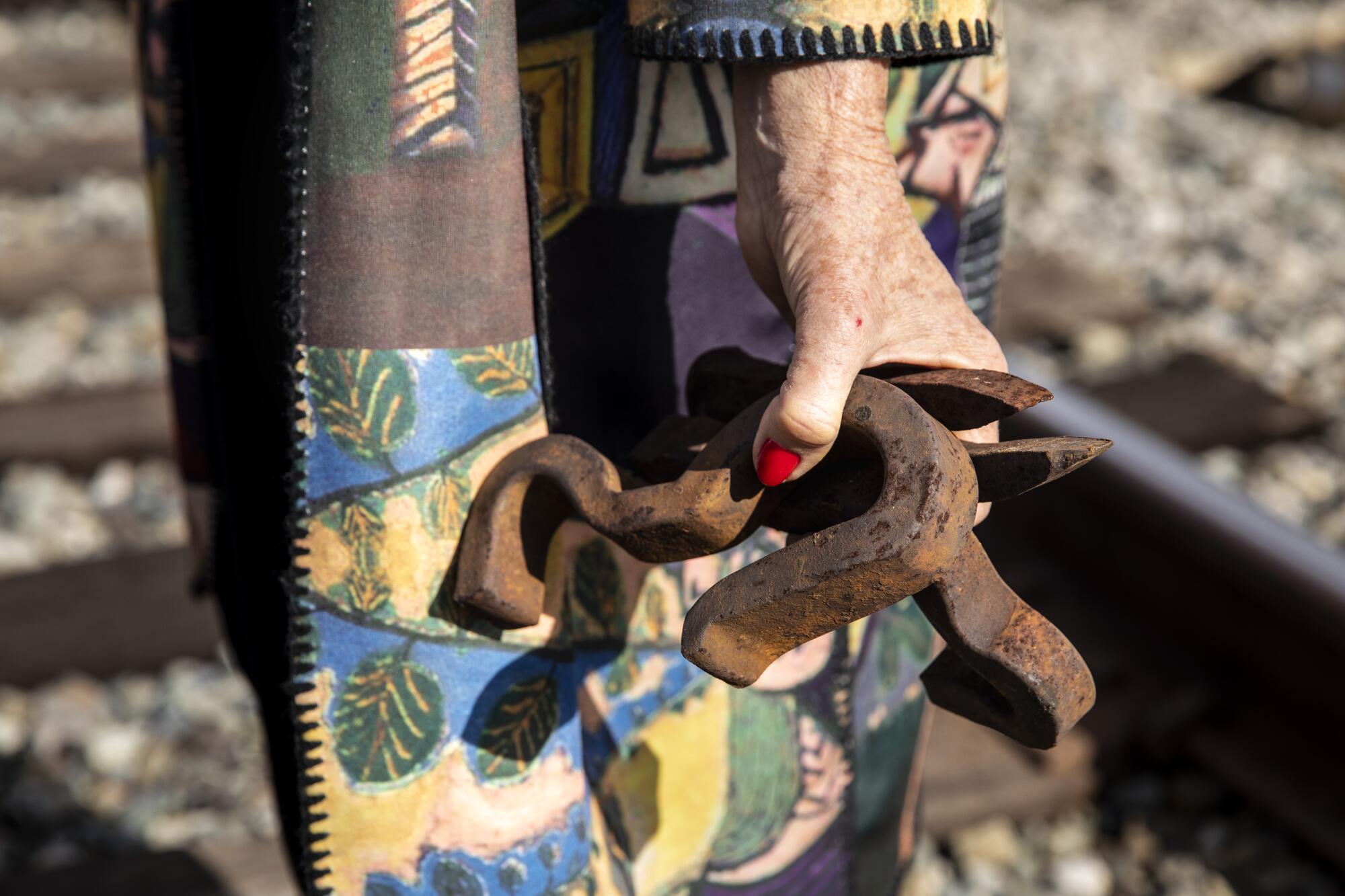 A closeup of a woman's hands holding rusted railroad spikes