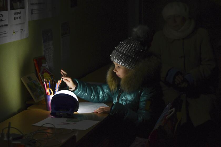 Alexandra, 11, draws at a school building, a "Point of Invincibility," a government-built help station that allows to charge phones with help of generators, serves food, drinks and the possibility to warm up, in Kramatorsk, Ukraine, Monday, Dec. 5, 2022. (AP Photo/Andriy Andriyenko)