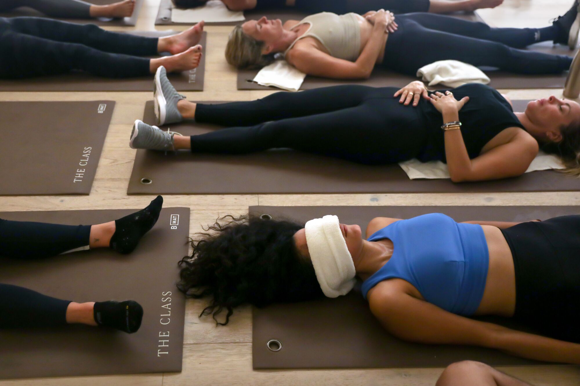 People lying flat on their backs upon yoga mats, one woman with a towel over her eyes