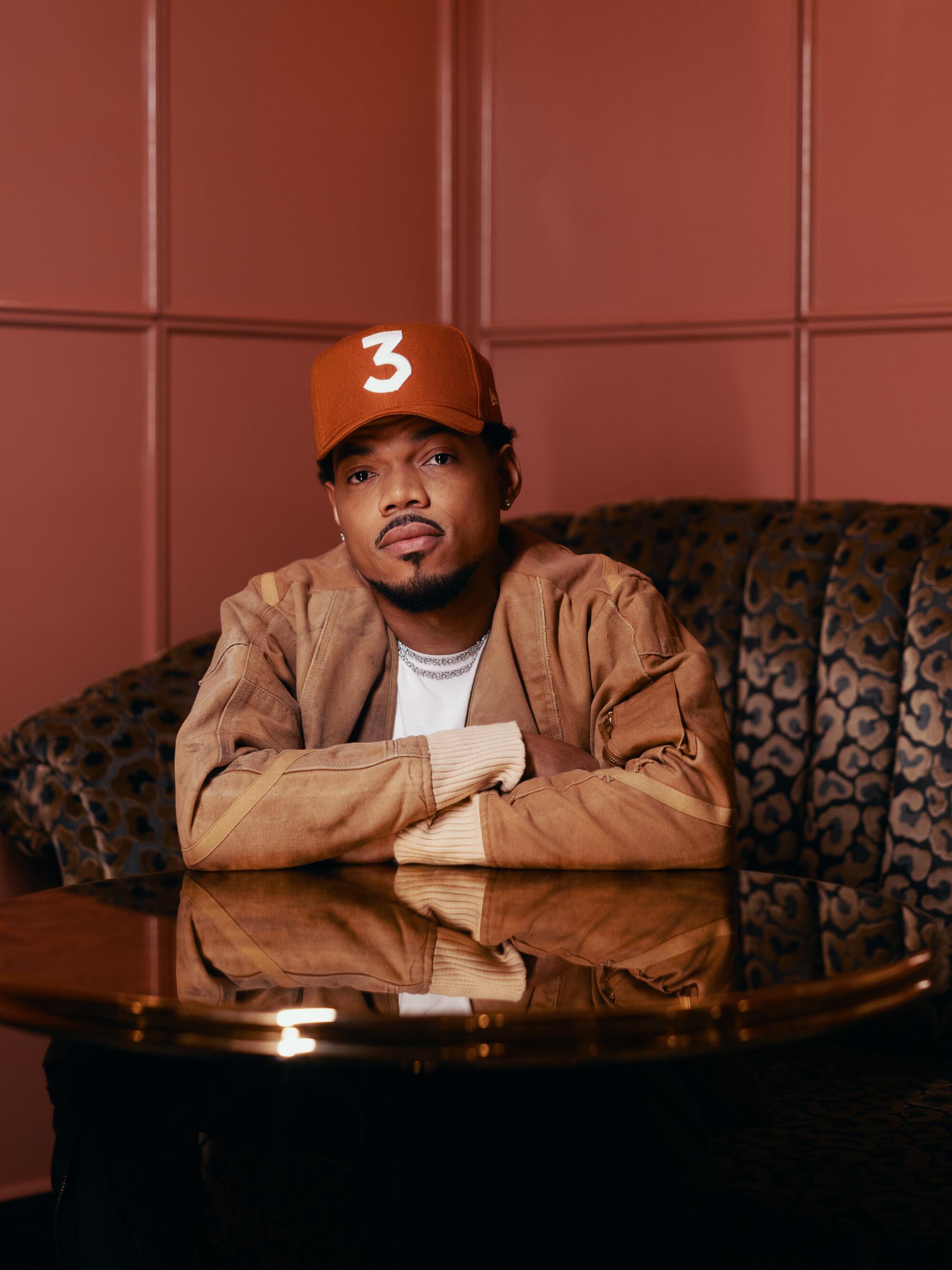 A man in a brown jacket and a red baseball cap with the number 3 on it sits at a booth.