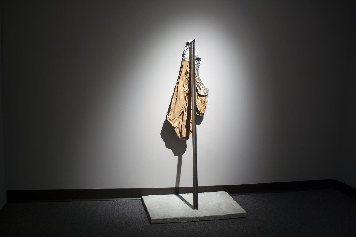 A dramatically illuminated photograph shows a woman's shirt held up by a steel fence post against a wall