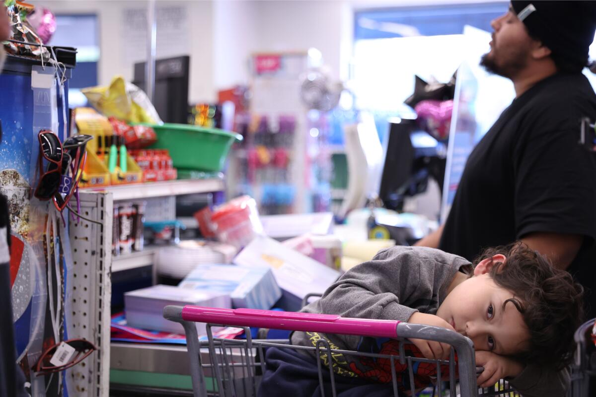 A boy rests his head on a shopping cart at a 99 Cents Only store as his father stands nearby.