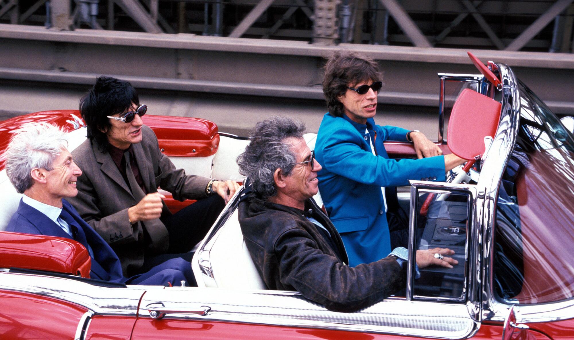 Mick Jagger drives Charlie Watts, Ron Wood and Keith Richards in a convertible car.