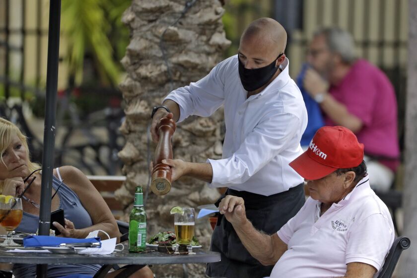 A food server wearing a protective face mask waits on customers at the Parkshore Grill restaurant Monday, May 4, 2020, in St. Petersburg, Fla. Several restaurants are reopening with a 25% capacity as part of Florida Gov. Ron DeSantis' plan to stop the spread of the coronavirus. (AP Photo/Chris O'Meara)