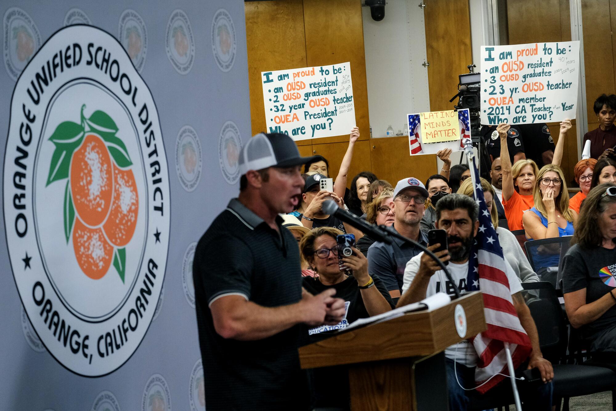 People hold up signs while a man addresses the Orange Unified School District board on Sept. 7.